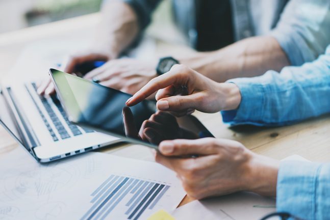 Team collaborating in modern office, using digital tablet for project planning. Young professionals working on startup in creative studio, with blurred film effect